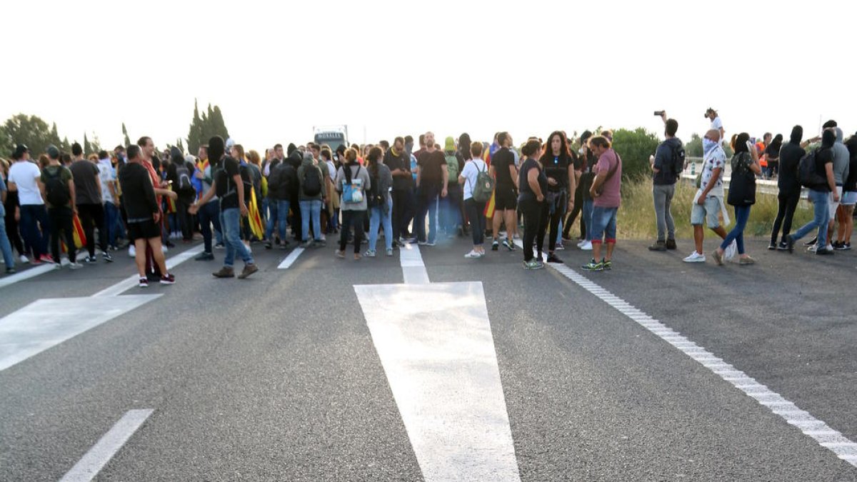 Primer pla de les senyals a l'asfalt de l'AP-7 a l'Ampolla amb els manifestants al fons. Imatge del 18 d'octubre del 2019 (vertical)