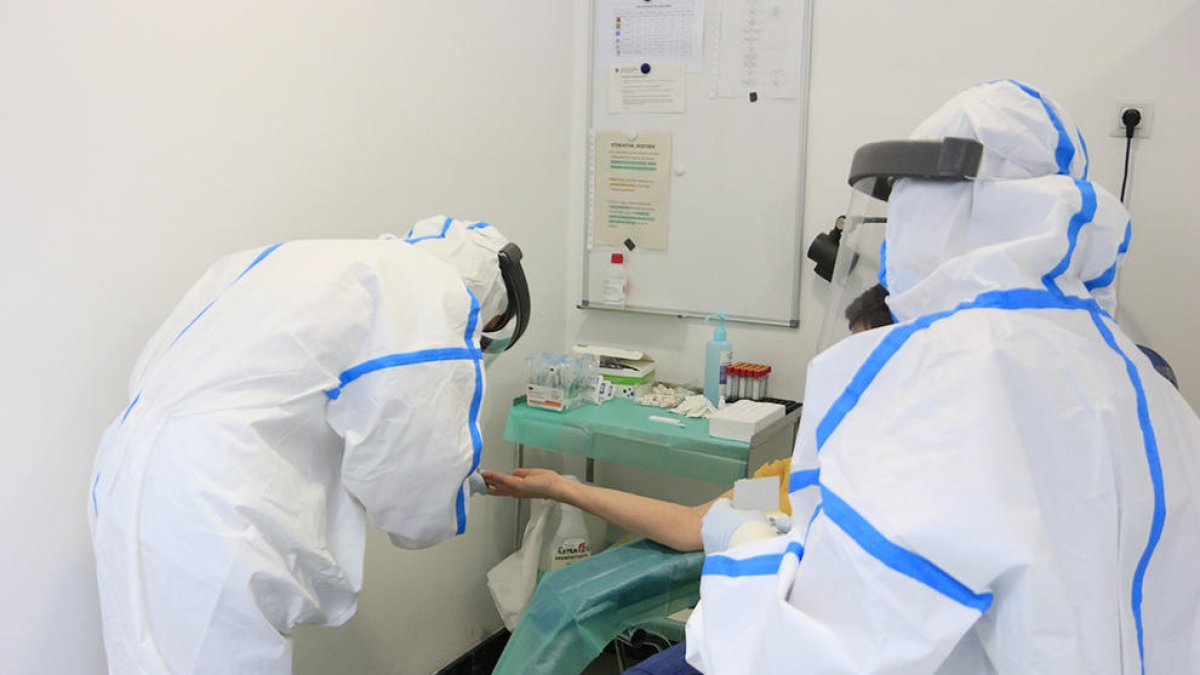 Professionals sanitaris, amb equip de protecció individual (EPI), en el moment d'extreure una mostra de sang amb una punxada al dit a una participant a l'estudi de seroprevalença del coronavirus a nivell estatal.