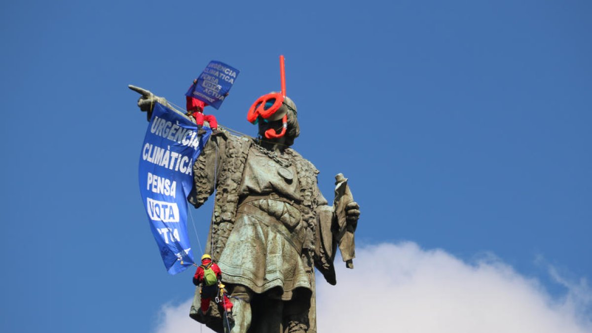 La estatua de Colón con dos activistas descolgando una pancarta.
