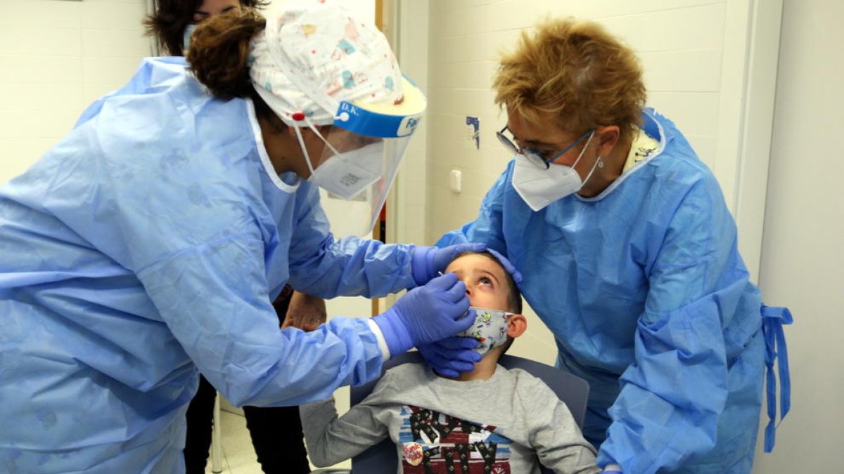 Imatge d'arxiu de dues infermeres fent un test ràpid d'antígens a un nen.