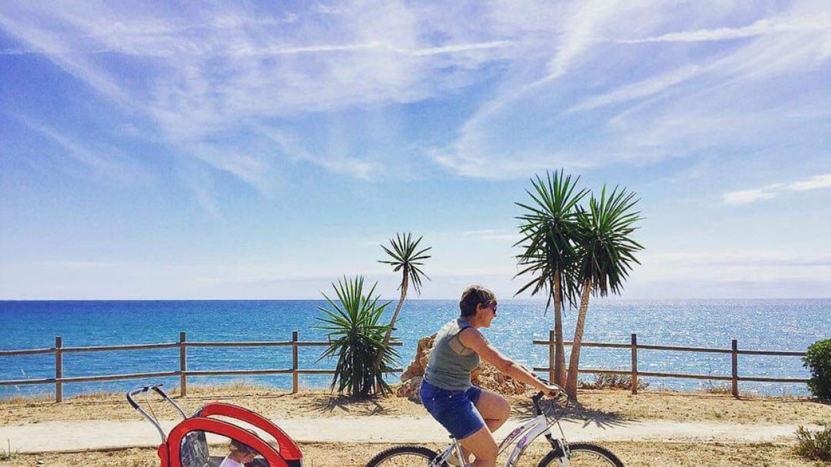 Pla general d'una dona amb bicicleta passejant un infant al municipi d'Alcanar