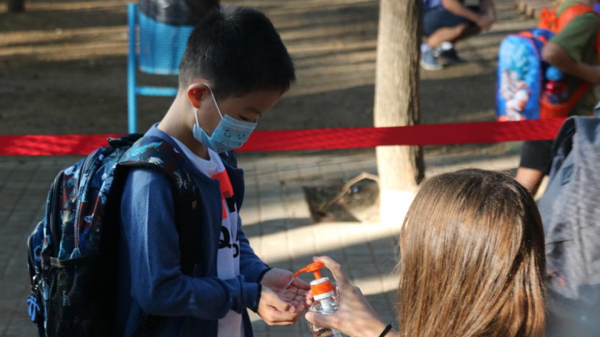 L'alumne d'una escola de Barcelona rebent gel desinfectant a l'entrada del centre.