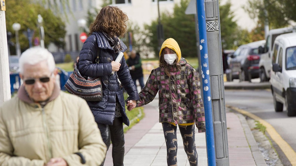 Una chica con máscara andando con su madre por la calle.