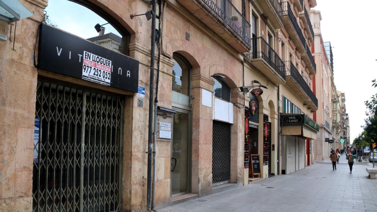 Una zona de la Rambla Nova de Tarragona on s'hi aprecien tres locals comercials buits, amb poc moviment de vianants.