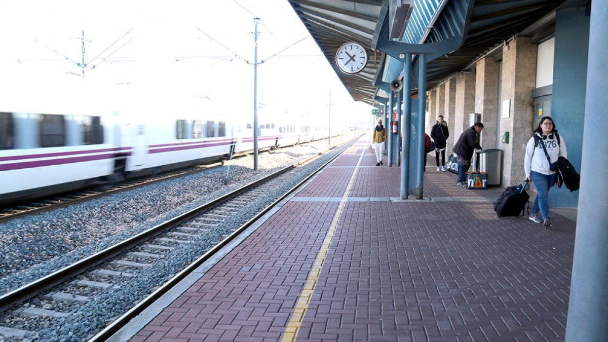 L'estació de l'Aldea-Tortosa-Amposta, amb viatgers a l'andana mentre un tren ràpid passa de llarg sense fer parada.
