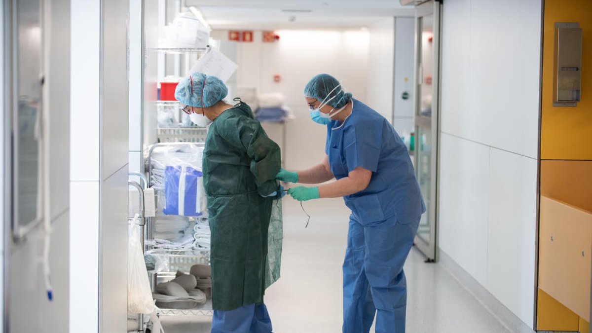 Una professional sanitària corda a una companya una bata abans d'atendre un pacient amb covid-19, en un dels blocs quirúrgics de l'Hospital Clínic de Barcelona habilitat com a UCI en la pandèmia de coronavirus.