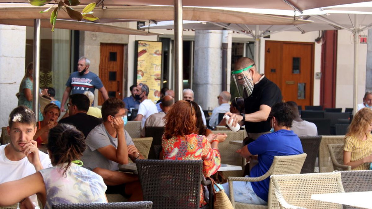 Un camarero de una terraza de la plaza del Ayuntamiento poniendo hidrogel a unos clientes.