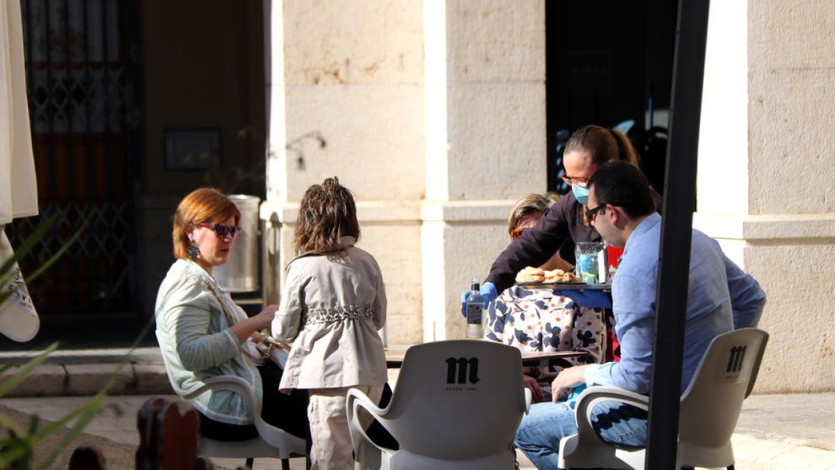 Una familia sentados en la terraza de un bar en Tortosa donde les sirven el desayuno.