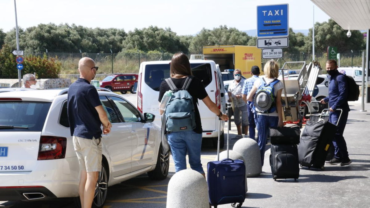 Plano general de turistas con maletas, esperando coger un taxi en el aeropuerto de Reus, después de aterrizar con el primer avión que llega a la capital del Baix Camp desde la alarma, proveniente del Reino Unido.