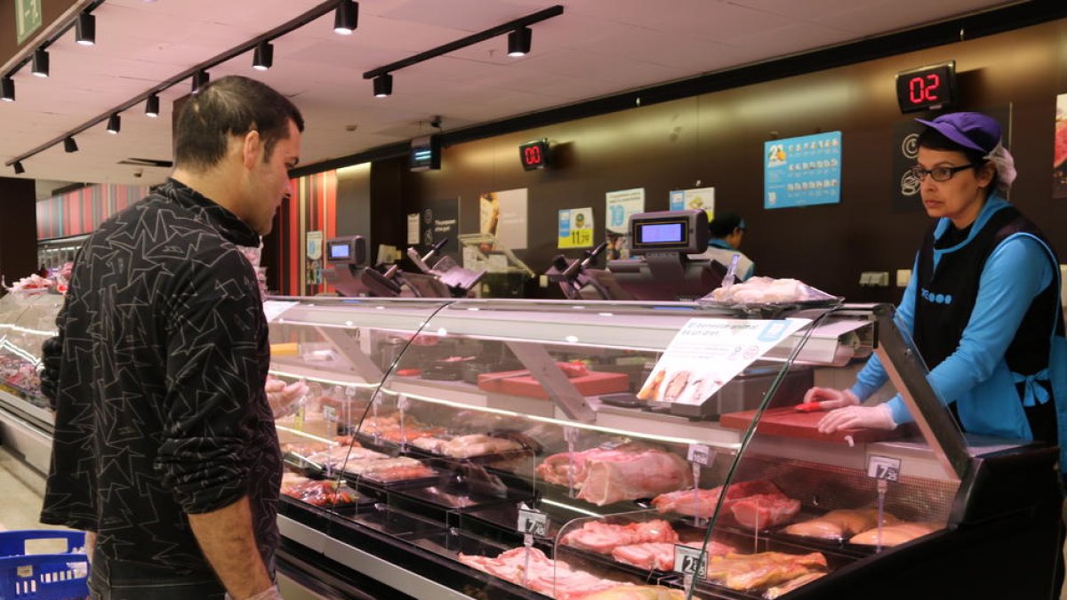 Un client amb guants comprant carn en un supermercat de l'Espai Gironès.