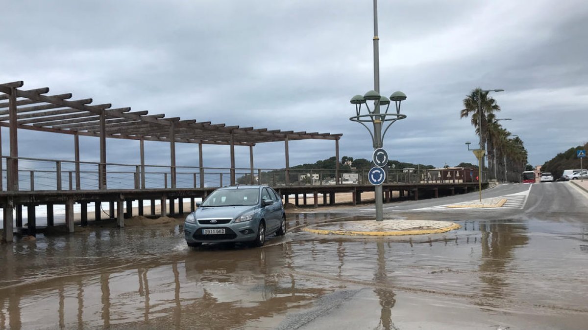 Un cotxe intentant passar per una rotonda amb tolls d'aigua de mar, a la platja de l'Arrabassada de Tarragona, a causa del temporal.
