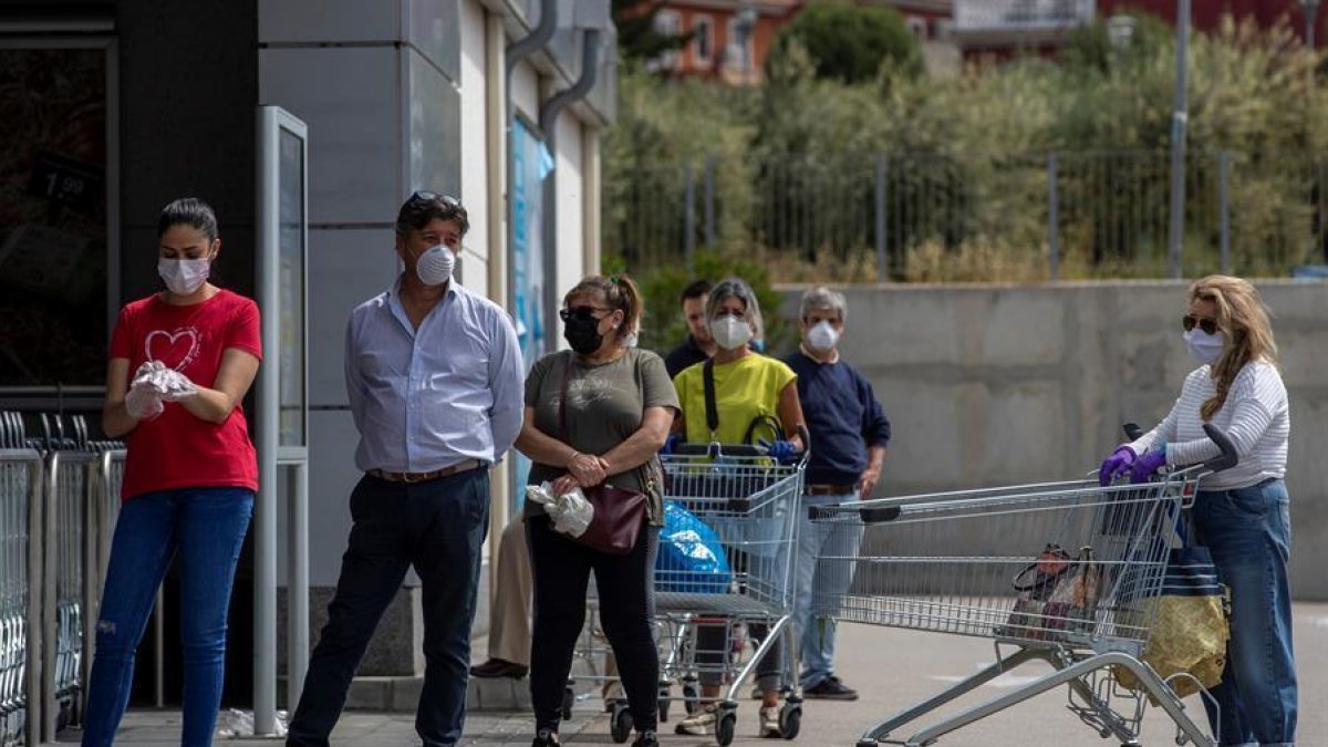 Diverses persones protegides amb mascaretes fan cua en l'entrada d'un supermercat.