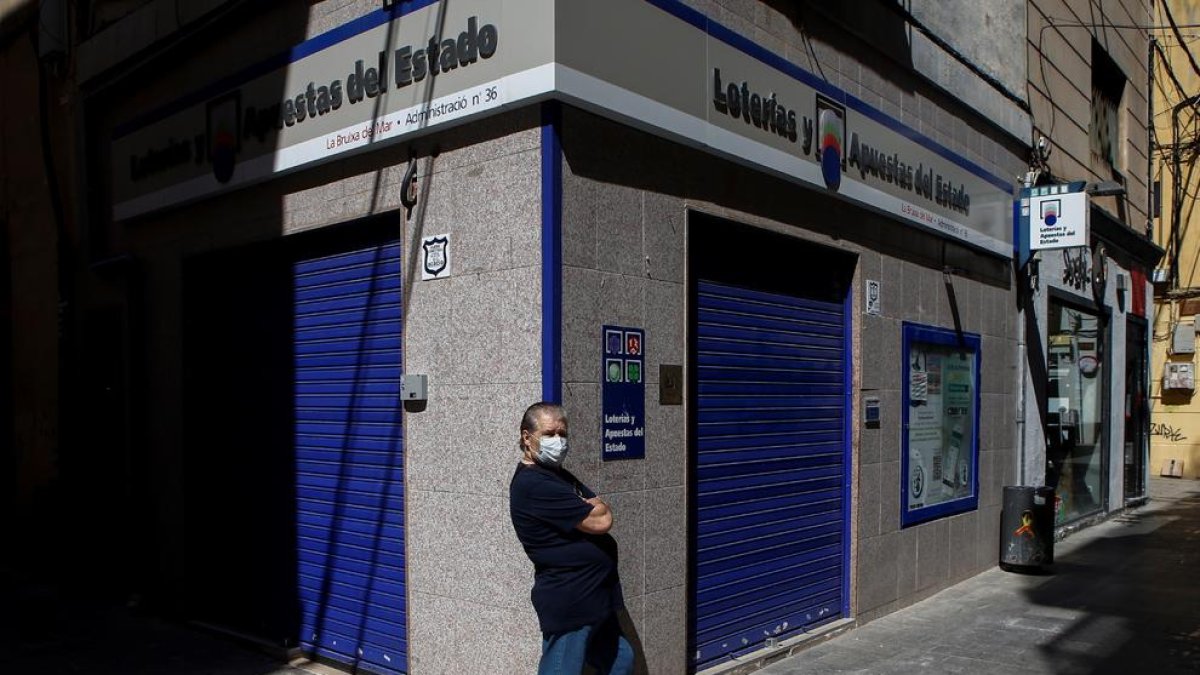 Un ciutadà transita enfront de l'edifici d'una administració de loteria al carrer de la Mar de Badalona (Barcelona)