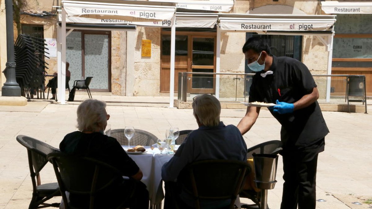 Dos clients d'esquenes i d'un cambrer servint els plats en una terrassa de la plaça de la Font