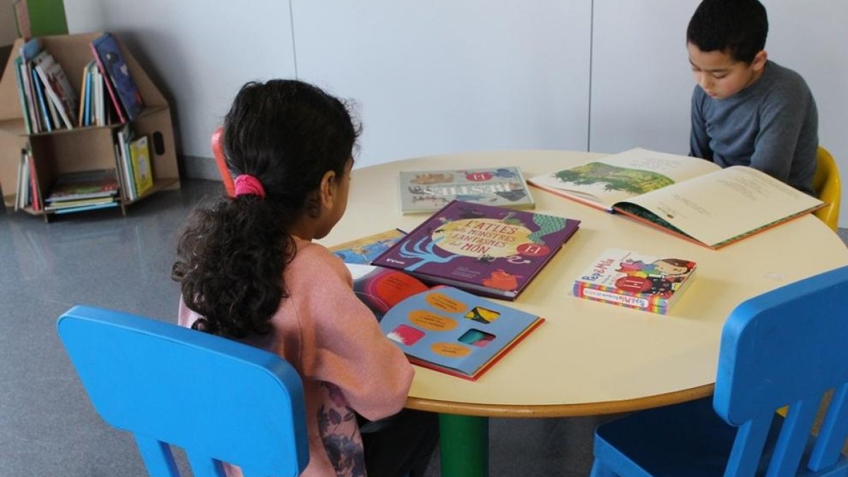 Imagen de dos niños disfrutando de libros en la nueva biblioteca infantil de las urgencias pediátricas del Hospital Joan XXIII.