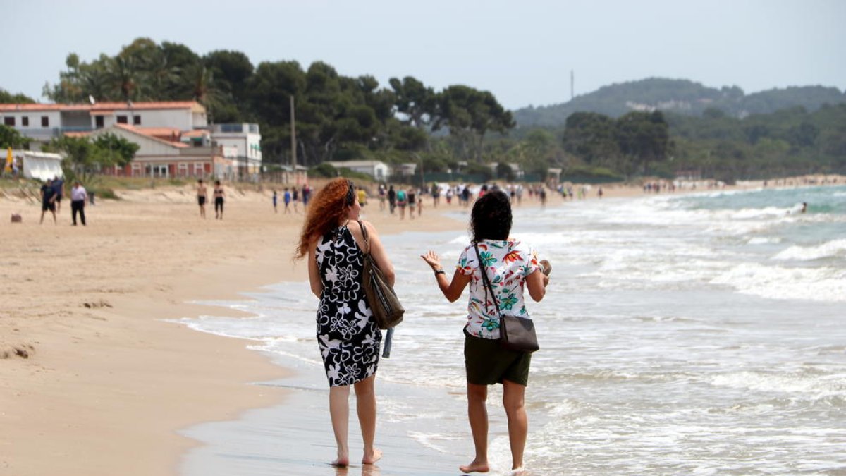 Dues dones d'esquenes caminant a la platja Llarga de Tarragona en l'últim dia de la fase 1.