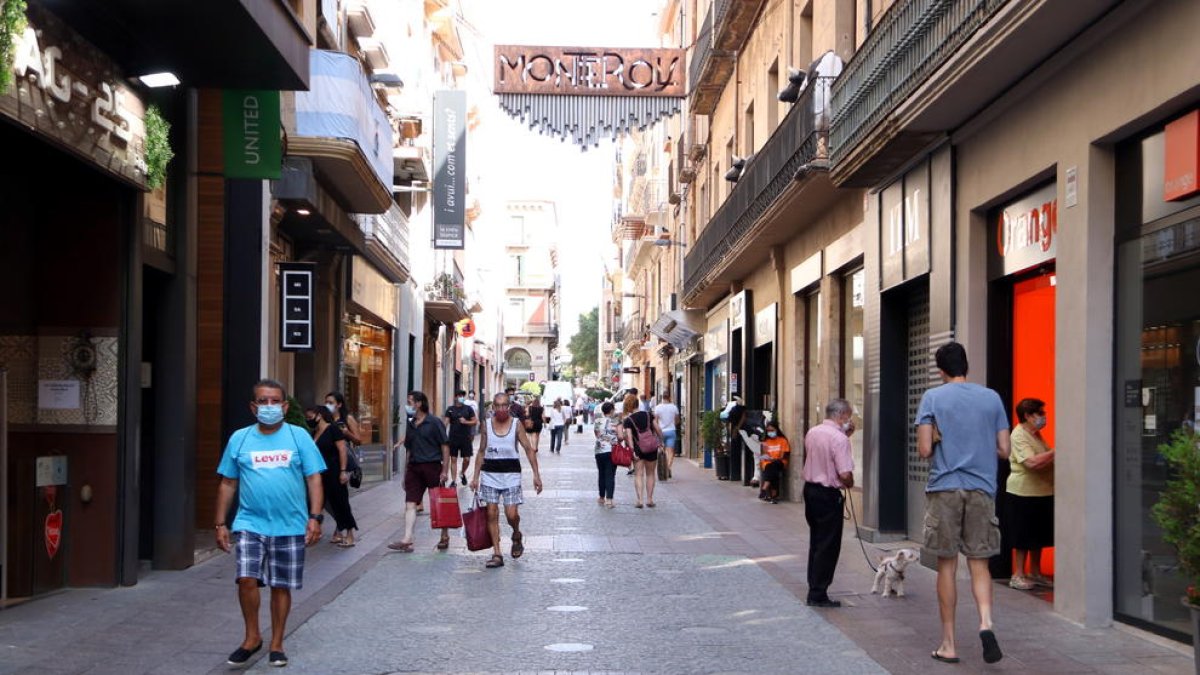 Plano general de varias personas con bolsas de compra en la calle Monterols de Reus.