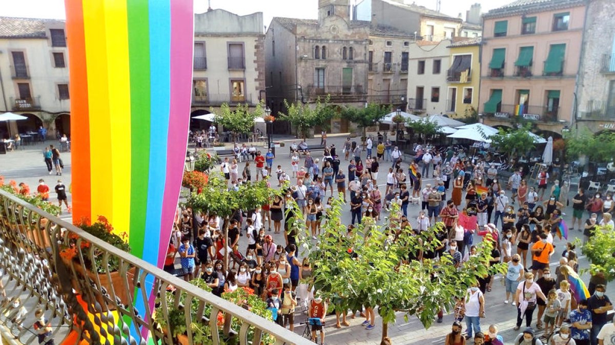 La plaça Major de Prades plena de persones concentrades contra l'homofòbia, amb la bandera LGTBI penjada en primer terme a l'Ajuntament.