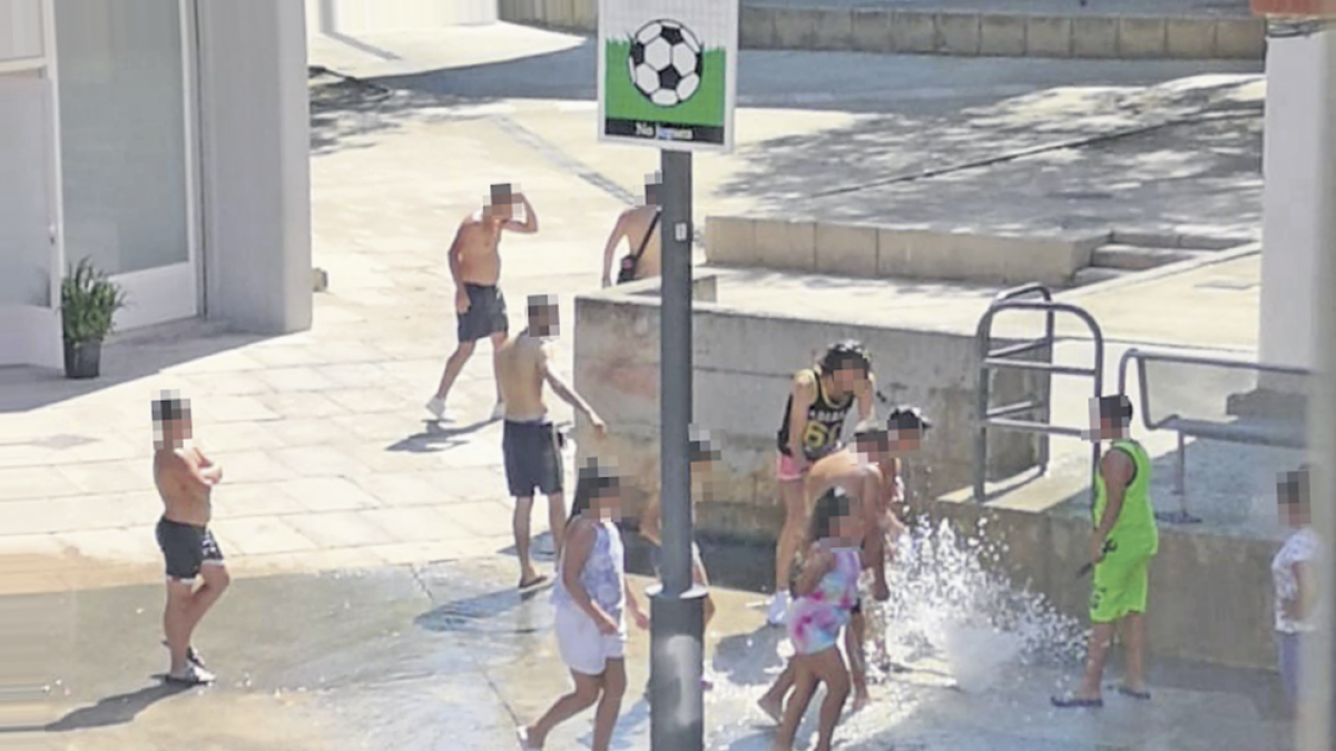 Un grupo se refresca con el agua a presión, en una plaza del barrio.