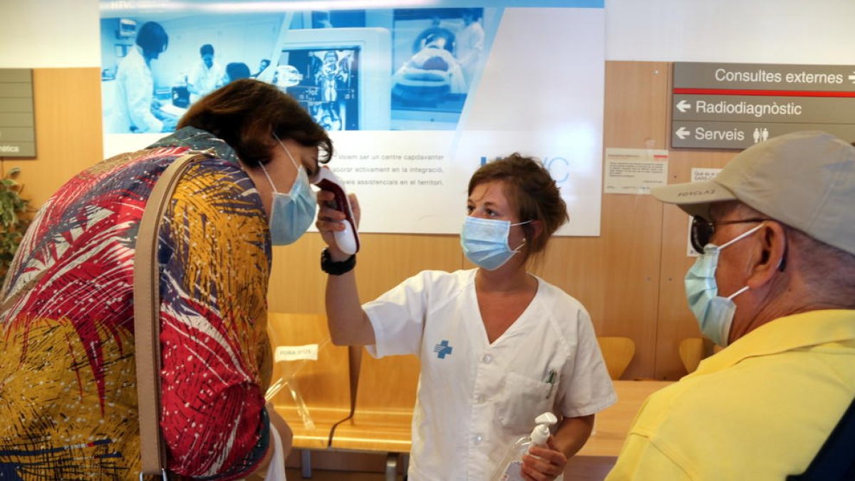 Una infermera prenent la temperatura a dos pacients abans que entrin a consultes externes de l'Hospital Verge de la Cinta de Tortosa.