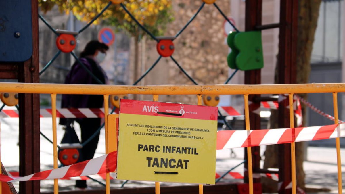 Cartell anunciant el tancament d'un parc infantil a Tortosa, on s'ha limitat l'accés amb tanques i cordons de seguretat.