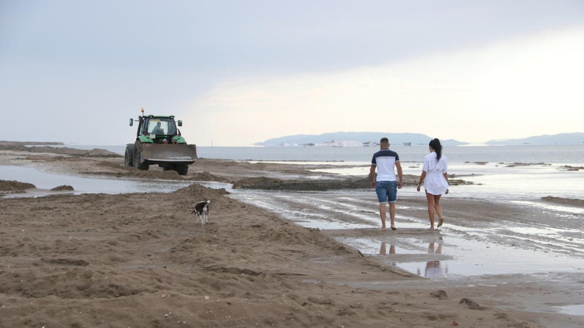 Dues persones i un gos caminant a prop d'una màquina treballant a la barra del Trabucador.