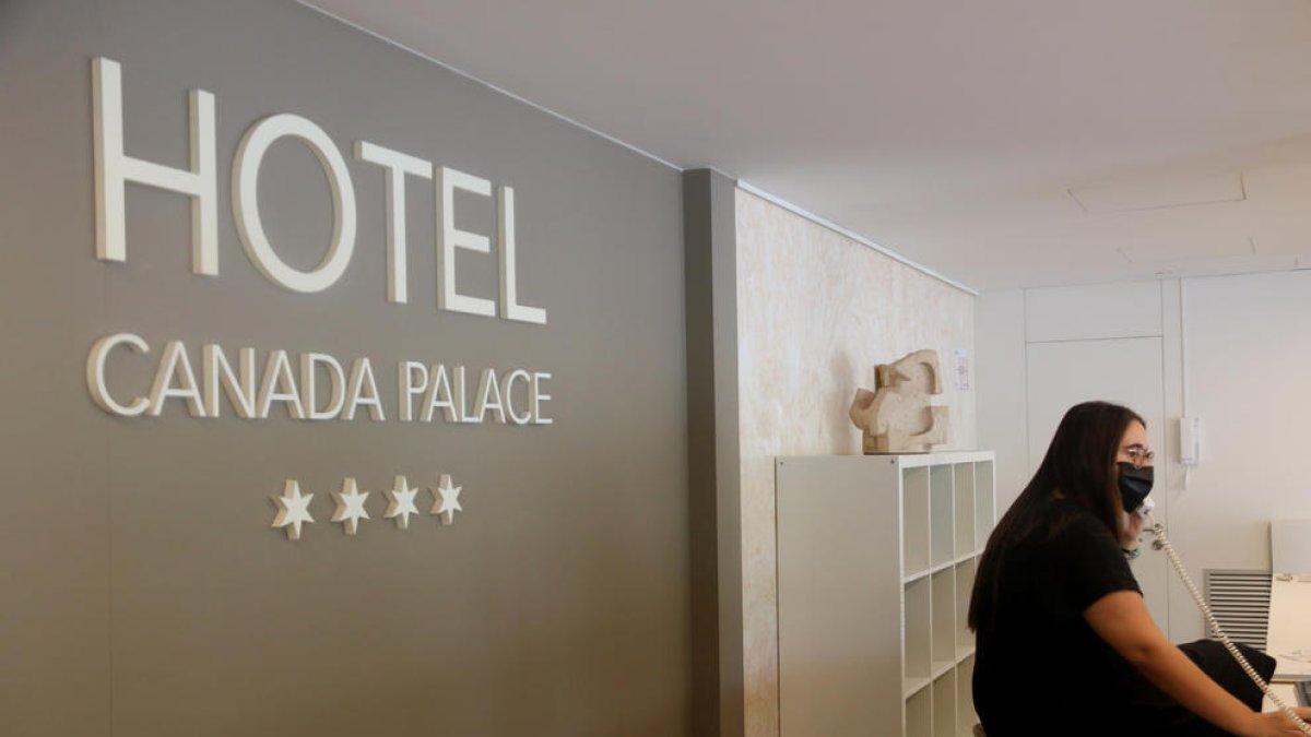 La recepció d'un hotel, amb una treballadora atenent el telèfon amb mascareta