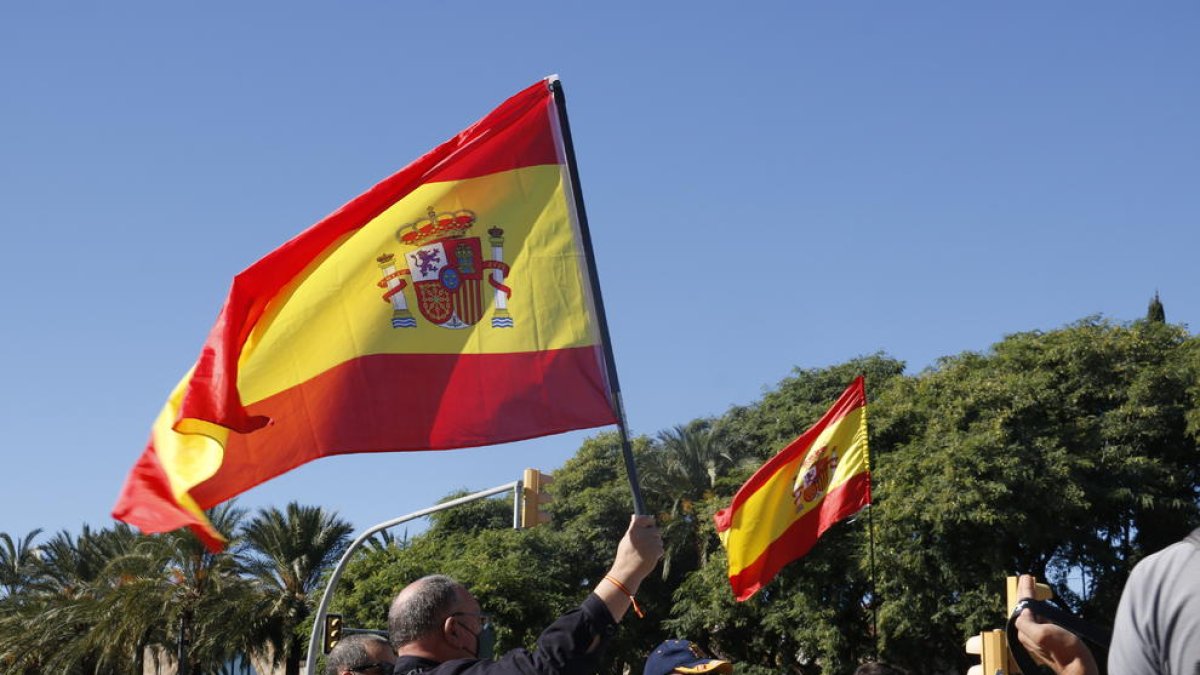 Unos manifestantes alzando banderas españolas durante la concentración en el monumento a Cristòfor Colom