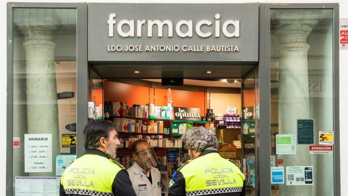 Dos agentes de la policía local de Sevilla a la entrada de una farmacia.