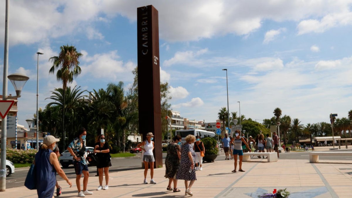 Turistas en el paseo marítimo de Cambrils, mirando interesados las flores y cirios en el suelo.