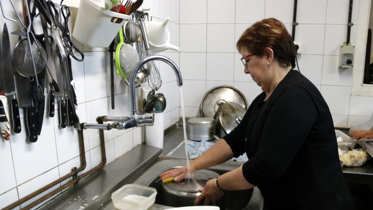 Pla general d'una dona de Castellolí mentre frega els plats amb l'aigua de l'aixeta.