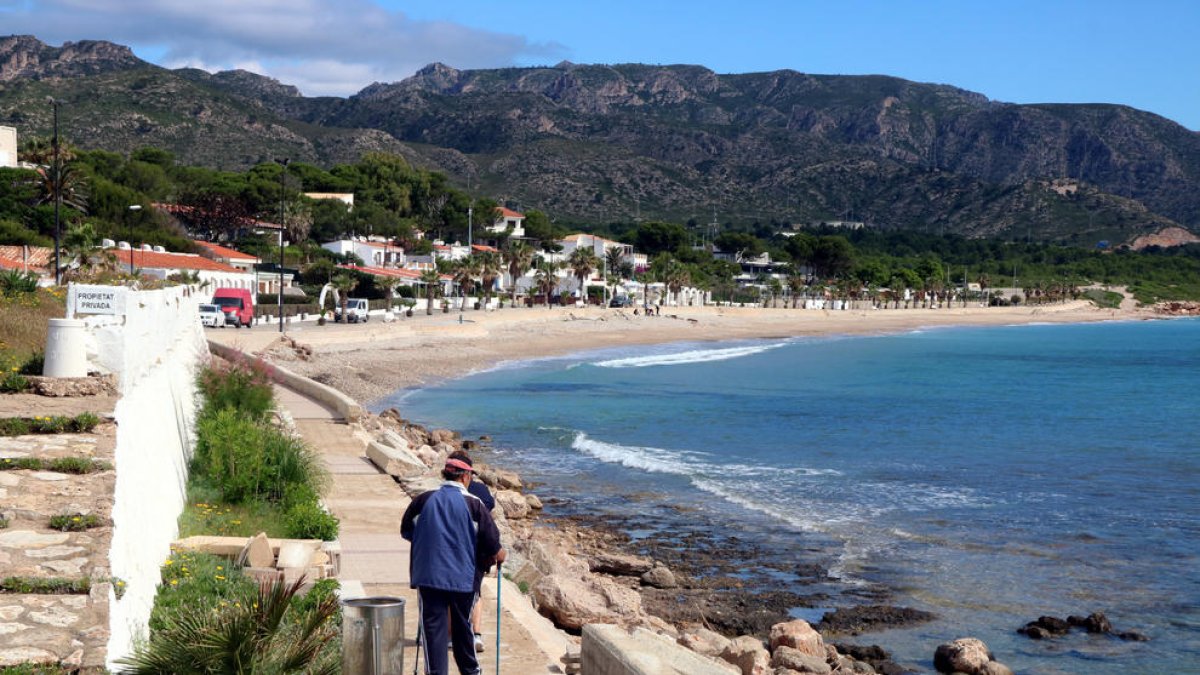 Plano general de dos personas que pasean en dirección a la playa de la Almadraba, en el municipio de Vandellòs i l'Hospitalet de l'Infant.