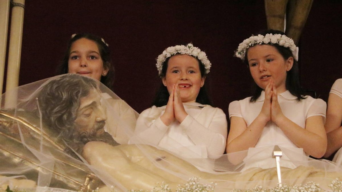 Plano medio de tres niñas vestidas de comunión durante la Coronación del Señor en Reus, delante del Cristo Ry..