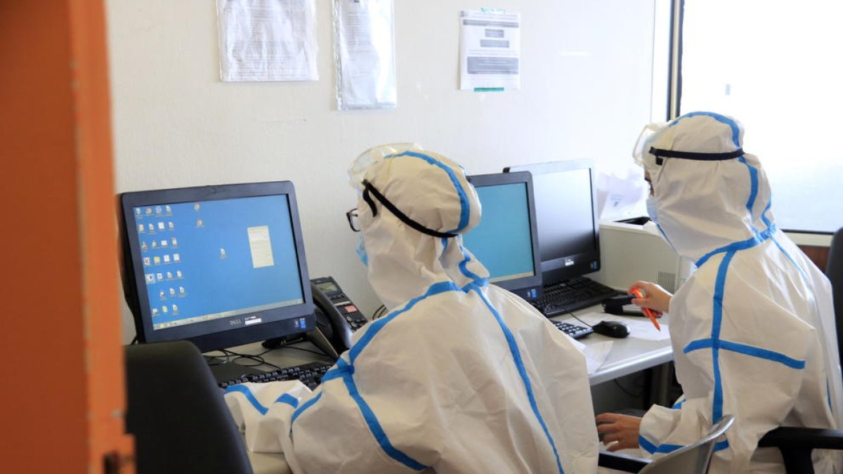 Dues metgesses amb l'equip de protecció individual pel coronavirus consultant informació de pacients amb covid-19 a l'ordinador, a l'Hospital del Mar.