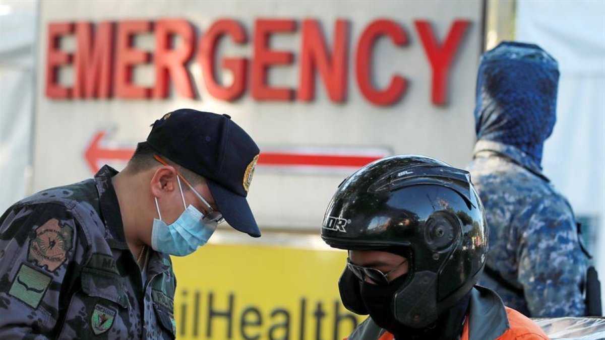 Un policía filipino con una mascarilla revisa un motorista en un puesto de control