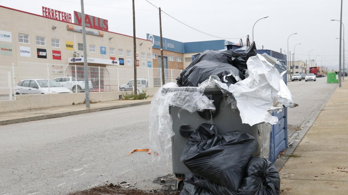 Contenedores llenos de basura y trastos en el polígono industrial de Valls, ante un negocio de una ferretería.