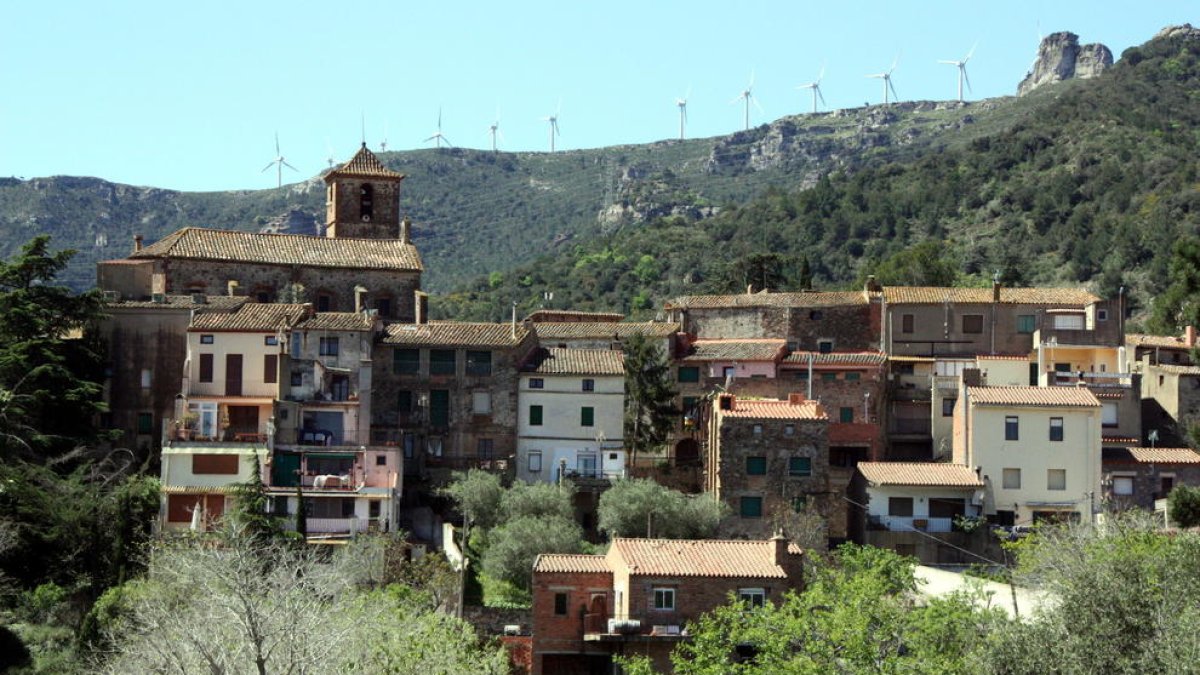 Pla general d'una panoràmica del poble de l'Argentera, al Baix Camp, amb l'església sobresortint d'entre els edificis i, al fons al darrere, molins d'energia eòlica damunt la muntanya