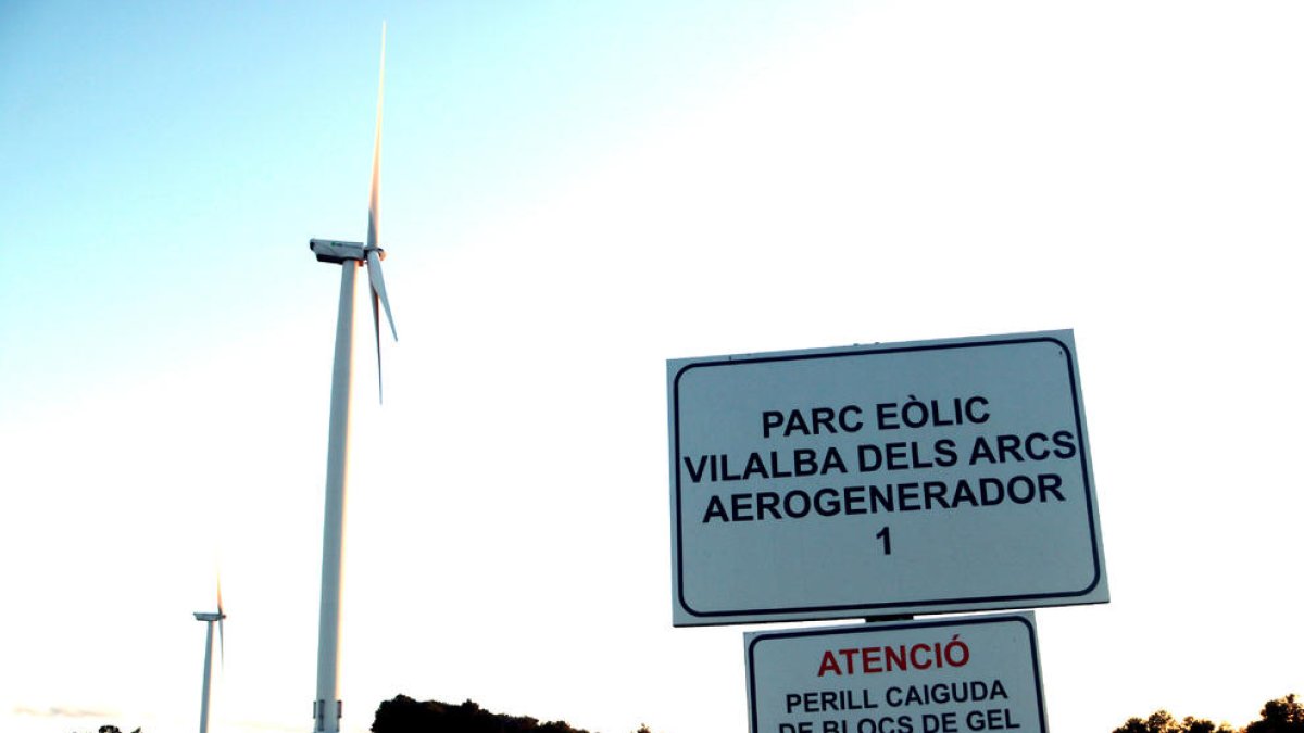 Un cartel señalizando un parque eólico en Vilalba dels Arcs, en la Terra Alta, con dos aerogeneradores en el fondo.