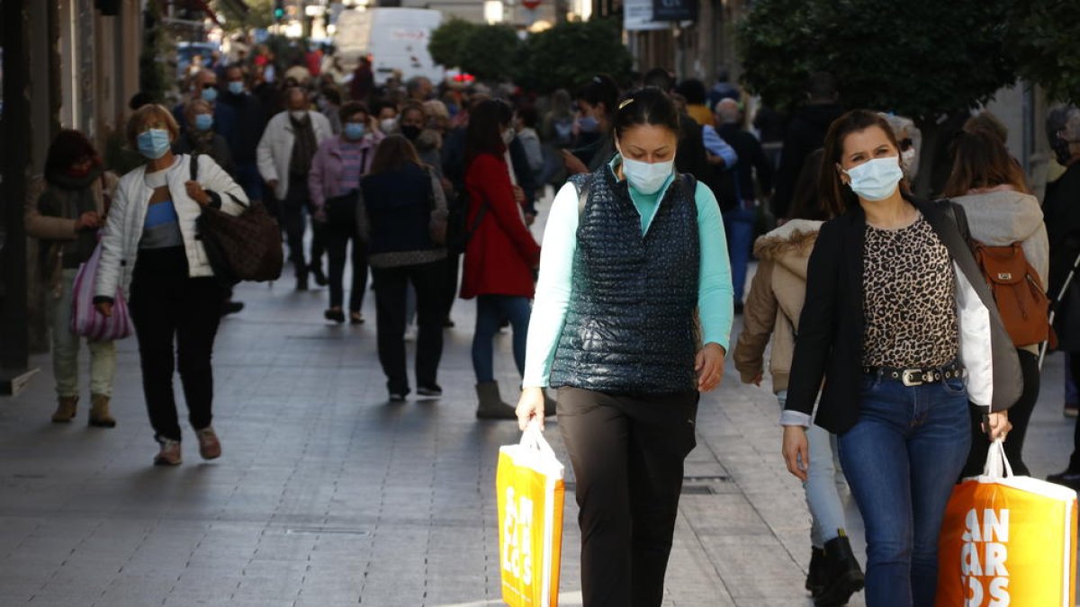 Unas chicas con bolsas, comprando en la calle de Llovera de Reus, en primer término, y en el fondo, gente paseando.