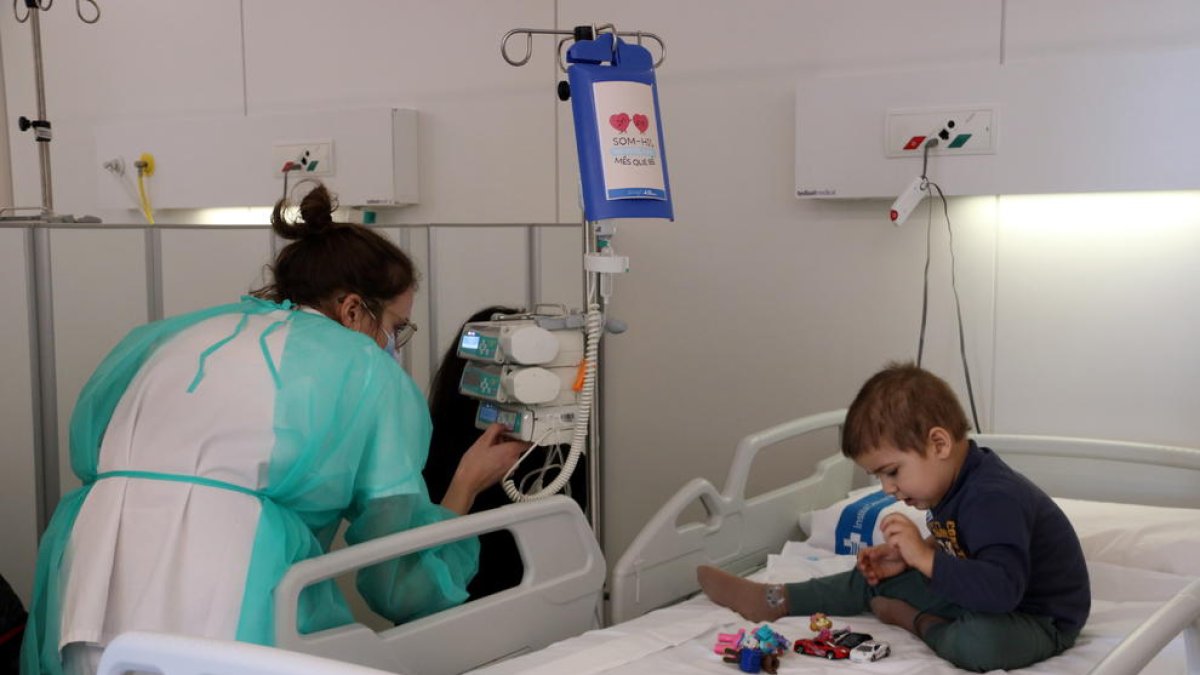 Una infermera supervisa la medicació a un nen a l'Hospital de Dia d'oncologia pediàtrica, on es pot veure la capsa de la medicació amb una il·lustració.