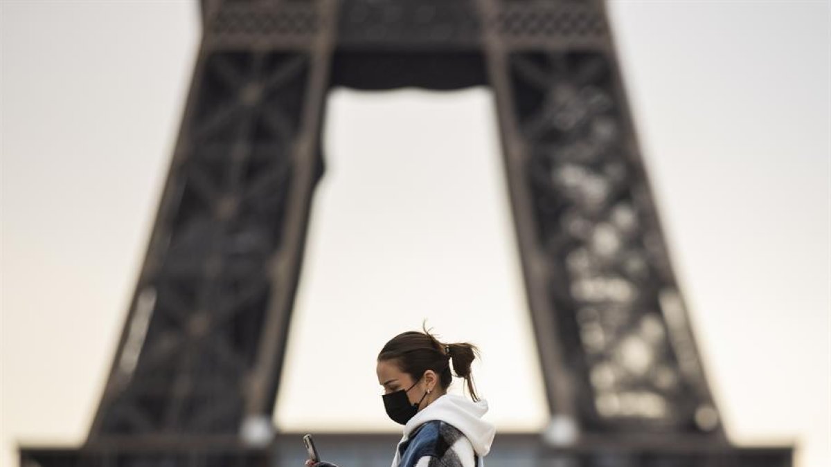 Una mujer con mascarilla pasando delante de la Torre Eiffel.