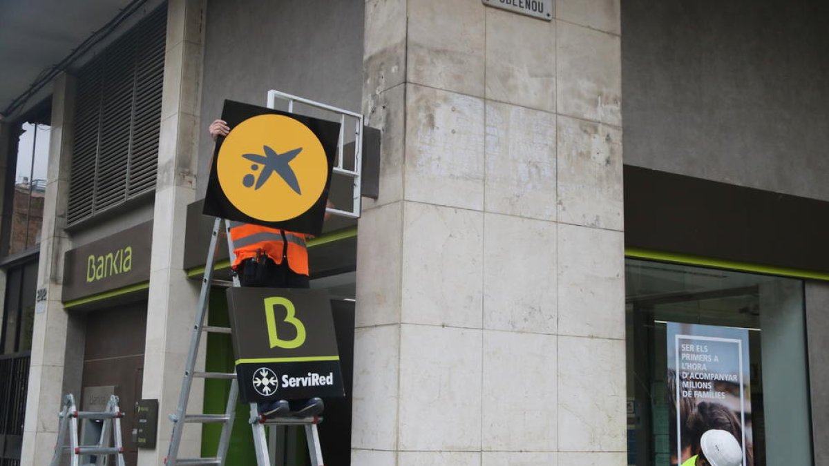 Un operario cambiando el logotipo de Bankia por el de CaixaBank en una oficina.