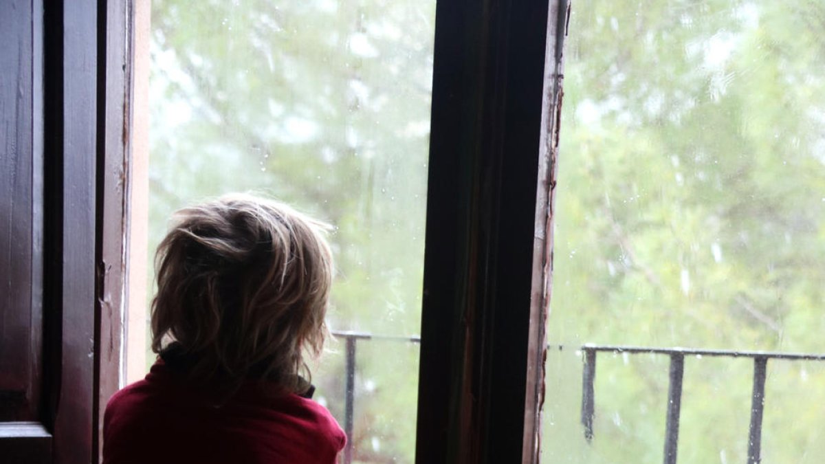 Un niño observa la nieve desde la ventana de su casa.