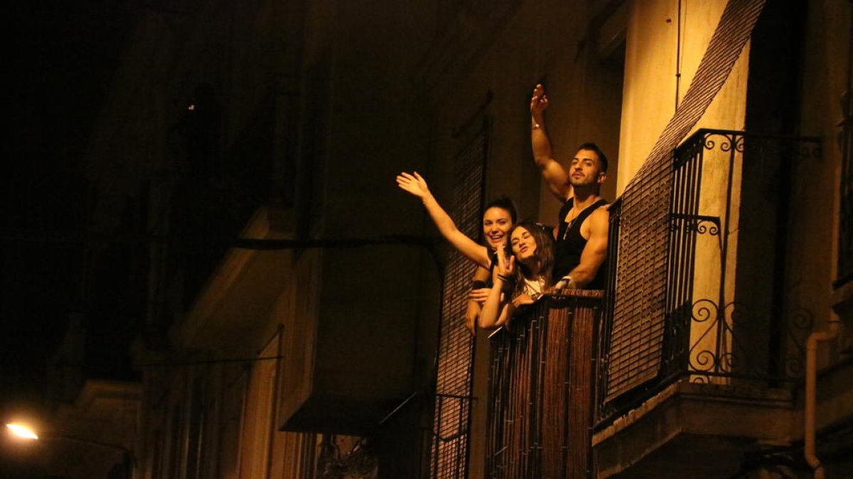 Tres jóvenes desde un balcón del barrio de Gracia celebran que acaba el toque de queda nocturno.