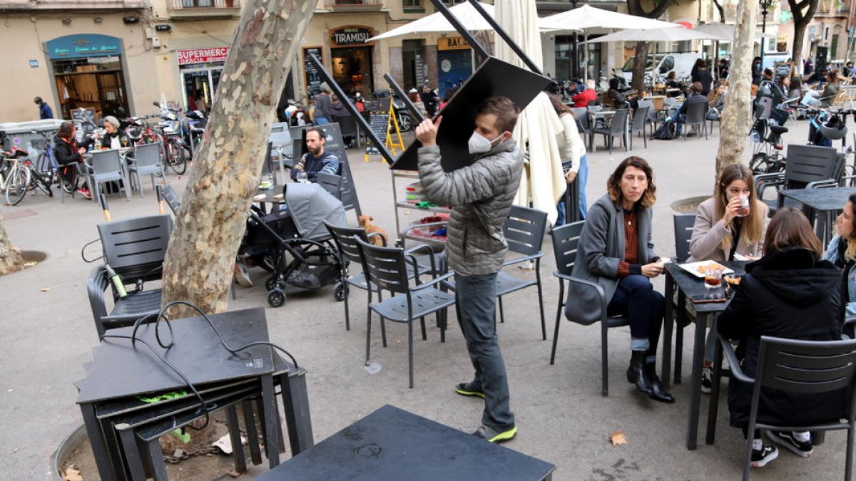 Uno trabajador de un restaurante recogiendo mesas y sillas con gente todavía comiendo.