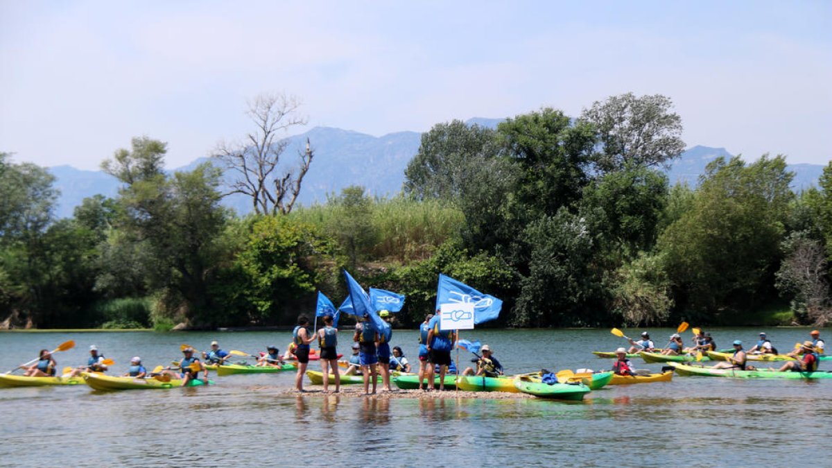 Els participants en la 20a Piraguada en Defensa de l'Ebre a la seva arribada a Tortosa, rodejant els activistes que han fet l'acció reivindicativa.