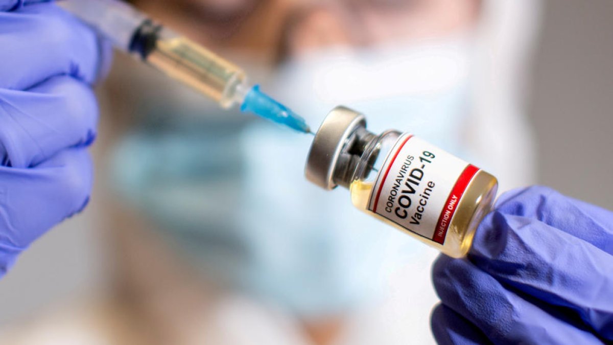 Una mujer tiene una jeringa médica y una botella pequeña con la etiqueta 'Vacuna contra el coronavirus COVID-19'
