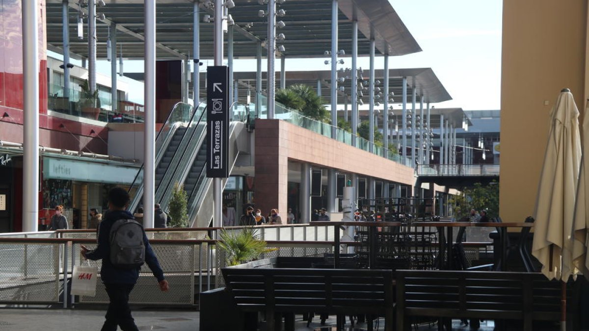 Un chico paseando por al lado de mesas y sillas retiradas en un punto del centro comercial La Maquinista.