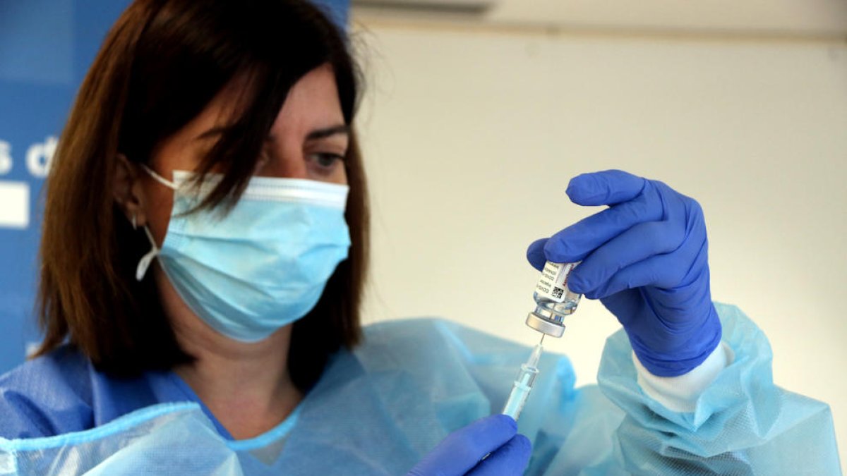 Una enfermera extrayendo las dosis de una botellita de la vacuna de AstraZeneca.