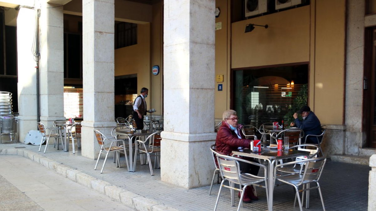 Ls terrassa del bar La Tertúlia de Tortosa amb alguns clients i el seu propietari servint-los.